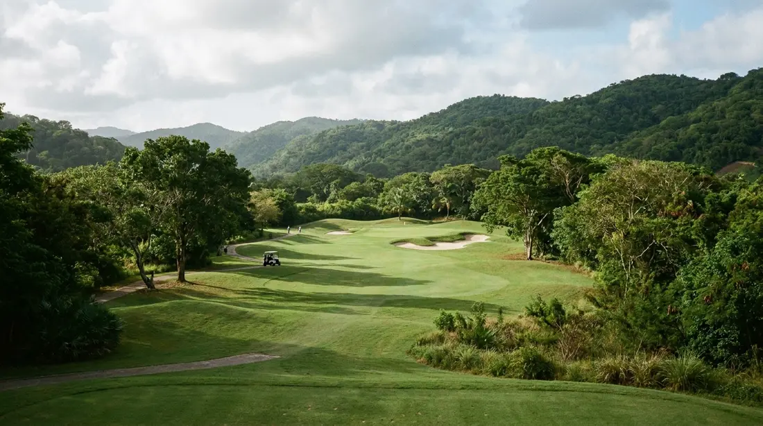 A fairway curving through a green valley toward a bunkered green