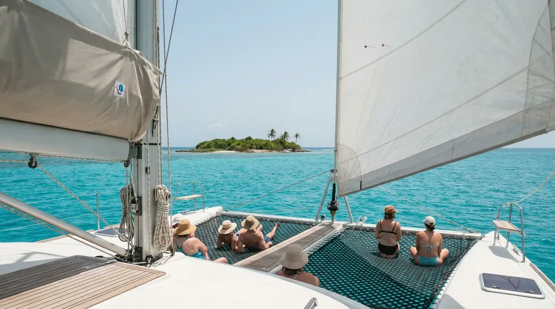 A catamaran under sail heading for a small green island