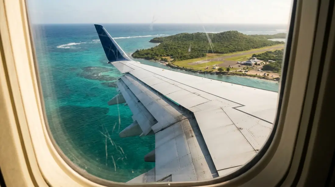 An aircraft wing over turquoise sea on approach to a green island
