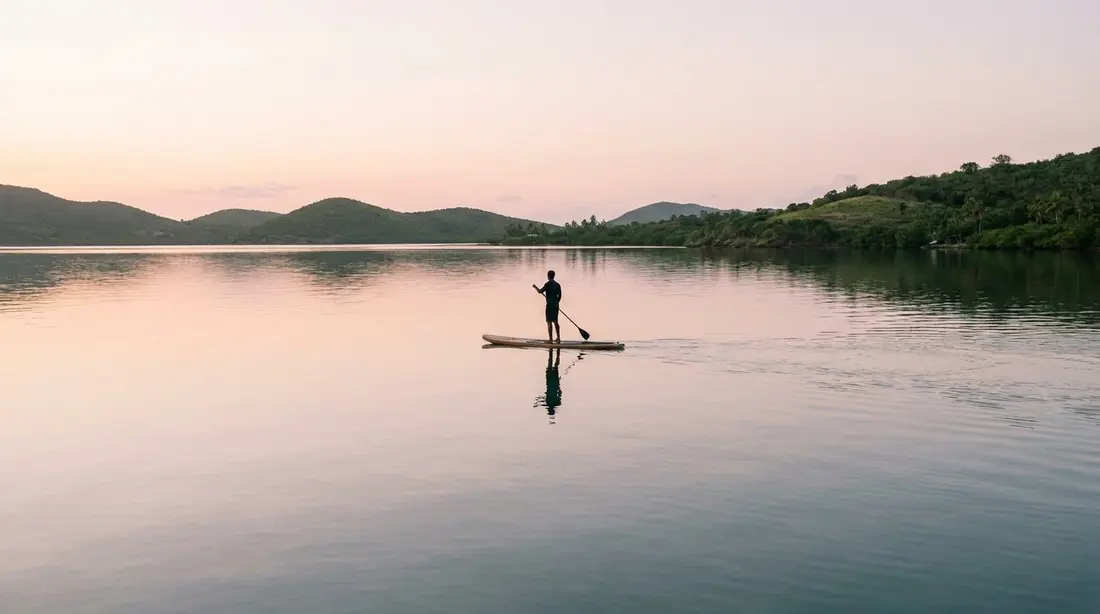 A paddleboarder on mirror-still water at dawn