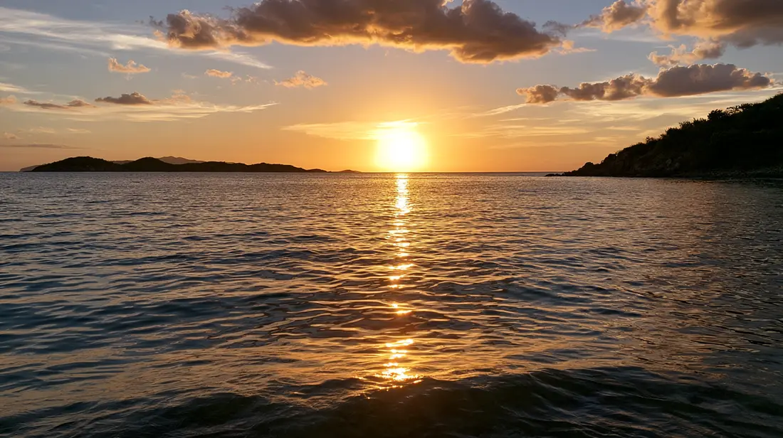 Sunset over calm water with a small cay on the horizon