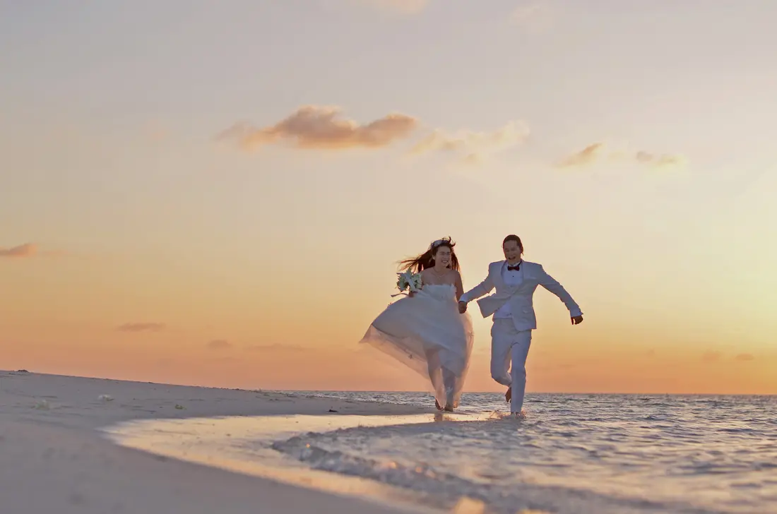 A couple in wedding clothes running along the sand at sunset