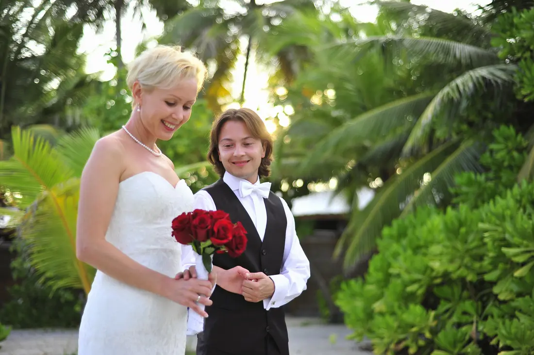 A bride and groom under the palms with a red bouquet