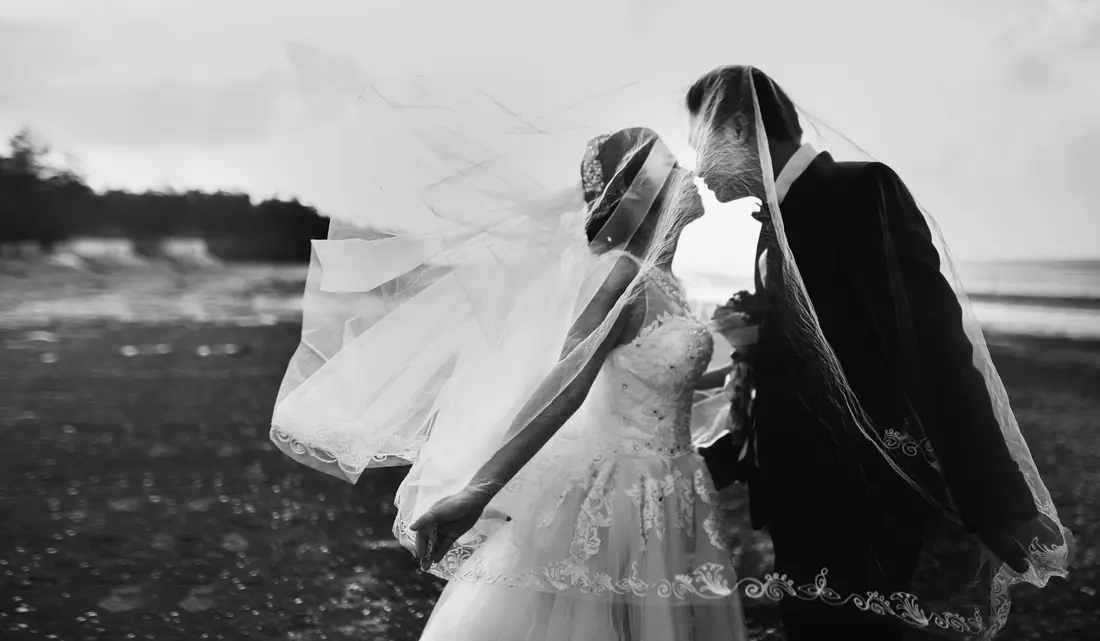 A bride and groom on a windswept beach, veil in the air